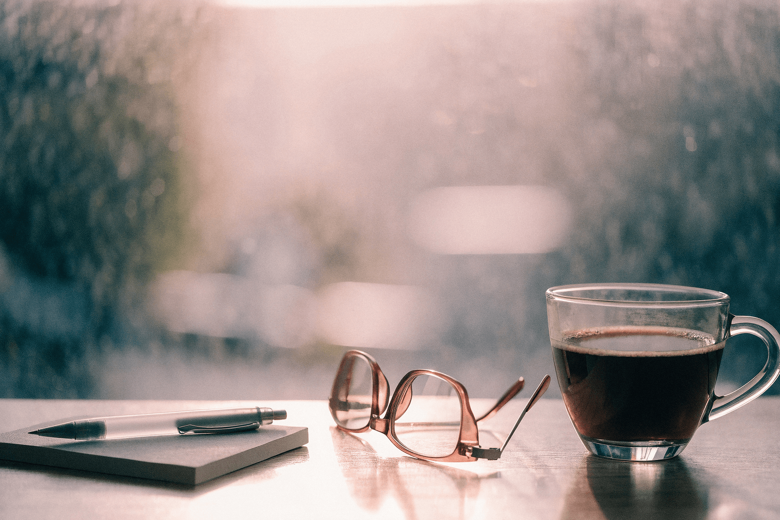 Mesa de manhã com café esfriando, óculos de leitura e bloco de notas diante de janela embaçada · a névoa mental da perimenopausa